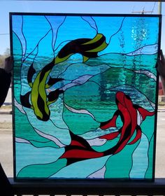 a person holding up a stained glass window with fish swimming in the water on it