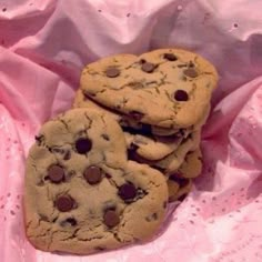 three chocolate chip cookies sitting on top of a pink cloth