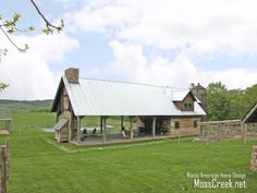 an old log cabin sits in the middle of a grassy field with picnic tables and benches