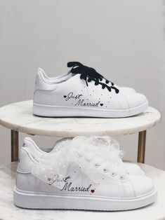 two white sneakers with black laces on them, one is decorated with hearts and the other has an inscription