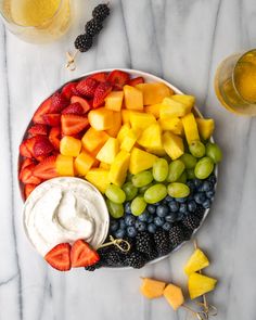 a plate filled with fruit and dips next to two glasses of beer on a marble table