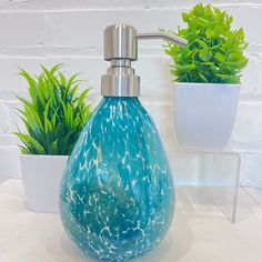 a blue glass soap dispenser sitting on top of a counter next to potted plants