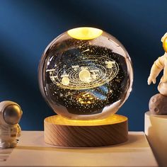 a glass globe with an image of the solar system in it and two small figurines next to it