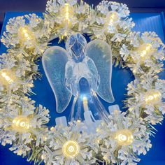 a christmas wreath with an angel on it and lights in the middle, surrounded by snowflakes