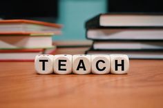 dice blocks spelling out the word teach on top of a wooden table with books in the background