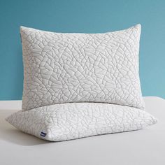 a white pillow sitting on top of a bed next to a blue wall with a plant in it