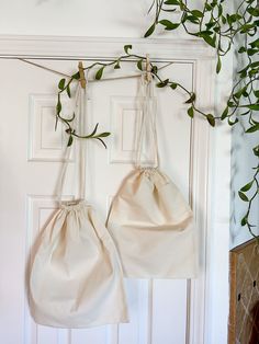 two white bags hanging on a wall next to a door with green plants in it