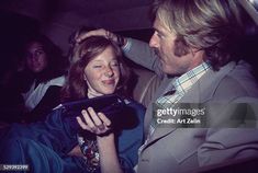 a man and woman sitting in the back seat of a car looking at an electronic device