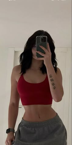 a woman taking a selfie with her cell phone in front of her face and wearing a red crop top