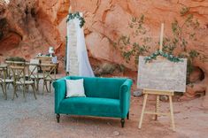 a blue couch sitting in the middle of a dirt field next to a wooden easel