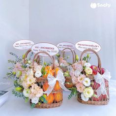 three baskets filled with fruit and flowers on top of a white table covered in signs