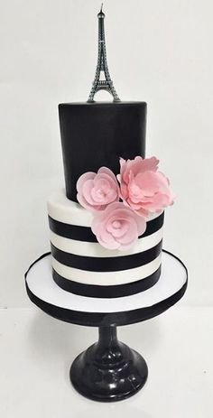 a black and white striped cake with pink flowers on top, in front of the eiffel tower