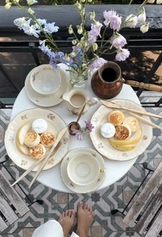 a table topped with plates and bowls filled with food next to a vase full of flowers