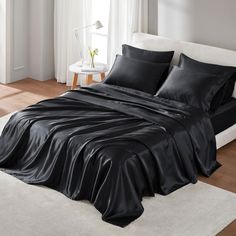 a bed with black sheets and pillows in a room next to a white rug on the floor