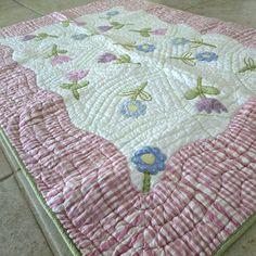 a pink and white quilted bed spread with blue flowers on the bottom, sitting on tile flooring