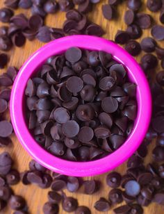 a pink bowl filled with chocolate chips on top of a wooden table