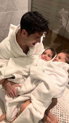 a man in a bathrobe holding a baby wrapped in a white towel and looking at the camera