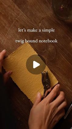 a person cutting paper with scissors on top of a wooden table next to a knife