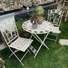 two white wrought iron patio furniture set with potted plants on the table and chairs