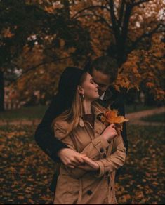 a man and woman standing next to each other in front of trees with leaves on them