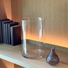 a glass vase sitting on top of a wooden shelf next to a bookcase filled with books