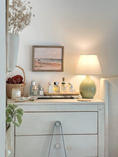 a white dresser topped with lots of items next to a lamp