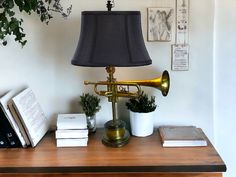 a brass trumpet lamp sitting on top of a wooden table next to books and plants