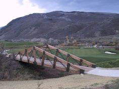 a wooden bridge over a small creek in front of a golf course with mountains in the background