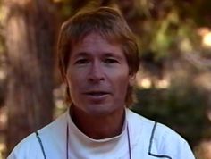 a man wearing a white shirt and necklace standing in front of trees