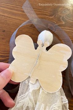 someone is making a paper angel decoration on a wooden table with ribbon and lace around it