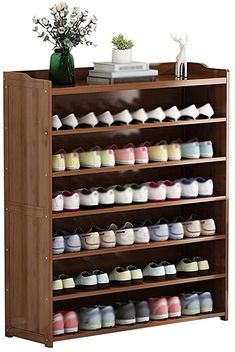 a wooden shoe rack with many pairs of shoes on the bottom shelf and flowers in vase next to it