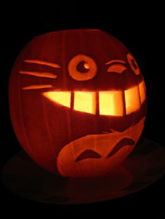 a pumpkin carved to look like a cat with glowing eyes and mouth is lit up in the dark