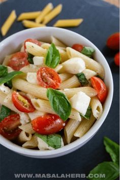 a white bowl filled with pasta, tomatoes and spinach on top of a table