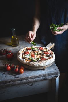 a person cutting up a pizza on top of a wooden table next to tomatoes and other vegetables