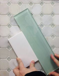 two hands are holding a white and green tile