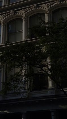 an old building with a clock on the side of it's face and trees in front of it