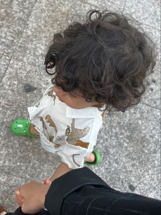 a toddler wearing a face mask and holding a green toy in his hand while sitting on the ground