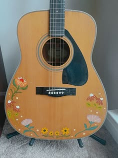 an acoustic guitar with flowers painted on the back and sides, sitting on a stand