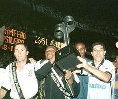 a group of men standing next to each other in front of a scoreboard holding up a trophy