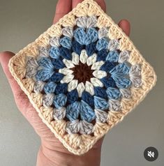 a hand holding up a crocheted square with blue and white flowers