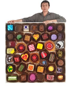 a man holding up a large chocolate box with many different types of candies in it