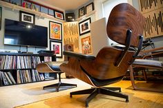 an eames chair and ottoman in front of a wall with pictures on the walls