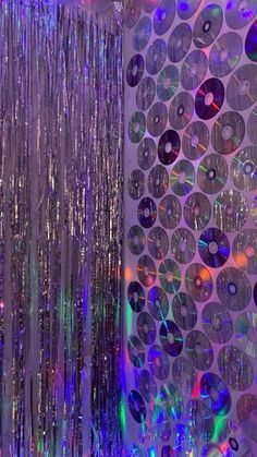 disco balls are hanging from the ceiling in front of a wall with many discs on it