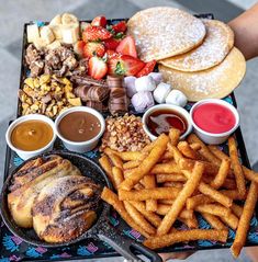 a person holding a tray full of food and dipping sauces on top of it