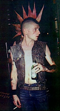 a man with spiked hair holding a beer in his hand and wearing a leather vest