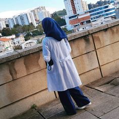 a person in a white coat and blue pants standing on a ledge looking at the city