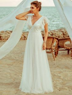 a woman standing on top of a beach next to the ocean wearing a white dress