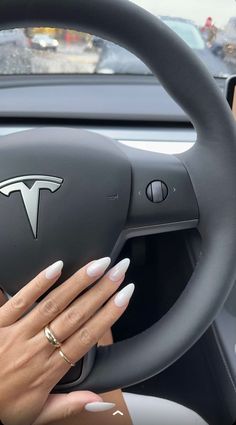 a woman driving a car with her hands on the steering wheel and nails painted white