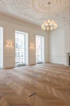 an empty room with chandelier, windows and wood flooring on the walls