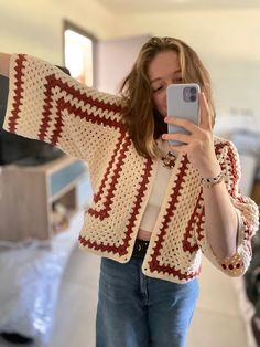 a woman taking a selfie with her cell phone while wearing a crocheted cardigan